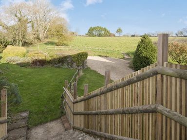 A garden with grass trees and a gravel path viewed from wooden stairs at The Gallery in Aveton Gifford