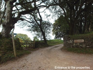 A dirt road entrance with a wooden gate and stone wall with trees surrounding at The Gallery in Aveton Gifford