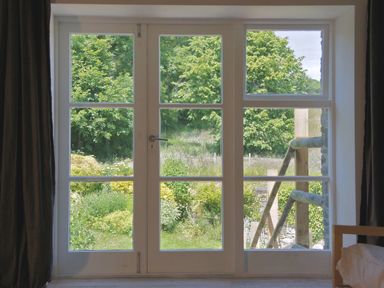 A window with glass panes overlooking a garden with green trees at The Gallery in Aveton Gifford