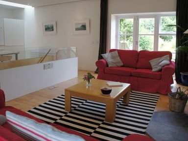 A living room with red sofas a wooden coffee table and glass doors leading outside at The Gallery in Aveton Gifford