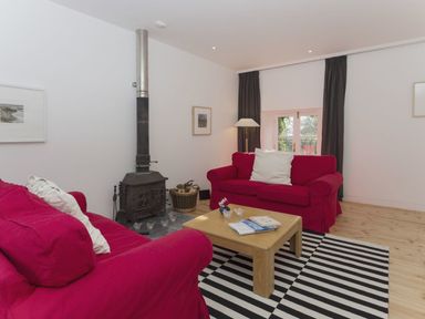 A living room with two red sofas a wooden coffee table a striped rug and a wood burning stove at The Gallery in Aveton Gifford