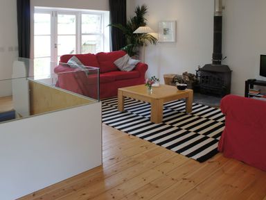 A living room with red sofas a wooden coffee table a striped rug and a wood burning stove at The Gallery in Aveton Gifford