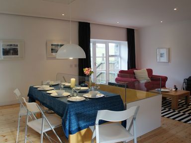 A dining table with blue tablecloth set with dishes and glasses near a living area with a red sofa at The Gallery in Aveton Gifford