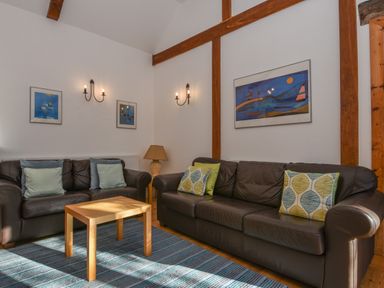 A living room with two brown leather sofas a wooden table a blue striped rug and wall art at Bradbridge Barn in Newton Ferrers