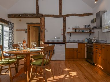 A kitchen with wooden cabinets and a round dining table set with plates glasses and a bottle at Bradbridge Barn in Newton Ferrers
