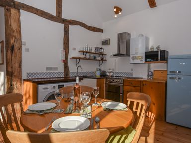 A kitchen with wooden cabinets a dining table set for four a blue fridge and open shelves displaying dishes at Bradbridge Barn in Newton Ferrers