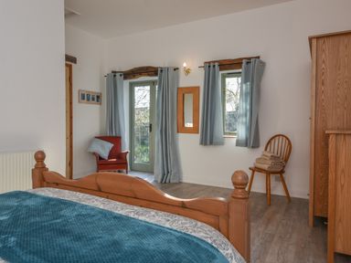 A bedroom with a wooden bed frame a red armchair blue curtains and a wooden chair with towels at Bradbridge Barn in Newton Ferrers