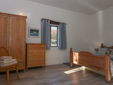 A bedroom with wooden wardrobe chest of drawers bed and a chair with towels at Bradbridge Barn in Newton Ferrers