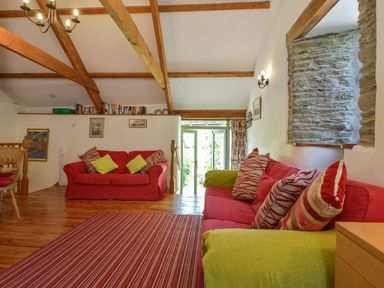 A living room with red sofas and striped cushions a striped rug wooden beams and a stone window at Parsonage Farm Cottage in Newton Ferrers