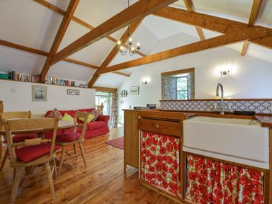 A kitchen and living area with wooden beams a red sofa wooden dining table and floral curtains at Parsonage Farm Cottage in Newton Ferrers