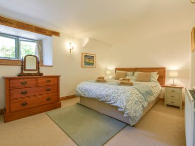 A bedroom with a double bed cushions bedside tables lamps a wooden dresser and a small window at Parsonage Farm Cottage in Newton Ferrers