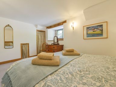 A bedroom with a bed with towels on it a dresser with a mirror a chair and framed artwork at Parsonage Farm Cottage in Newton Ferrers