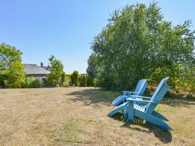 A garden with two blue wooden chairs on dry grass and trees in the background at Parsonage Farm Cottage in Newton Ferrers