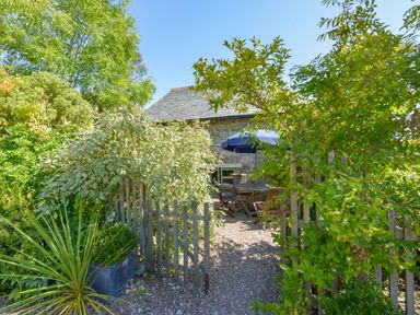 An outdoor garden area with wooden table and chairs under a blue umbrella and a stone building in the background at Parsonage Farm Cottage in Newton Ferrers