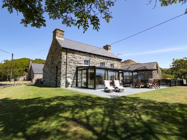 A stone farmhouse with glass sunroom and outdoor patio furniture on a lawn at Garth Morthin The Farmhouse in Porthmadog