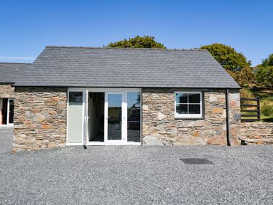 A small stone building with slate roof glass double doors and a window on a gravel ground at Garth Morthin The Farmhouse in Porthmadog