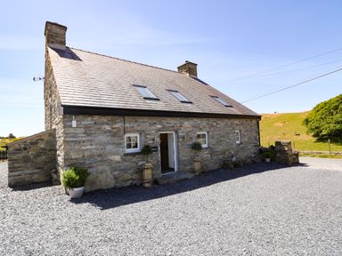 A stone farmhouse with a slate roof and gravel ground outside at Garth Morthin The Farmhouse in Porthmadog