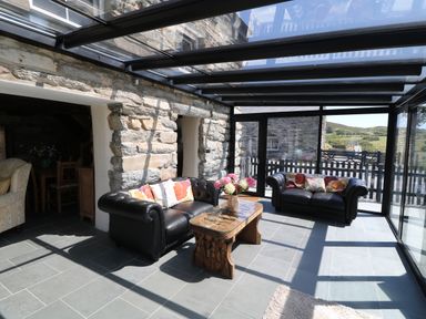 A sunroom with two black leather sofas and a carved wooden coffee table with flowers at Garth Morthin The Farmhouse in Porthmadog