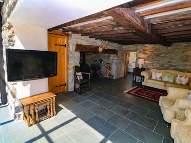 A living room with a mounted television small tables a fireplace chairs and sofas at Garth Morthin The Farmhouse in Porthmadog