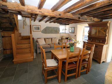A dining area with wooden table and chairs a sofa wooden stairs and a cabinet with mirror at Garth Morthin The Farmhouse in Porthmadog