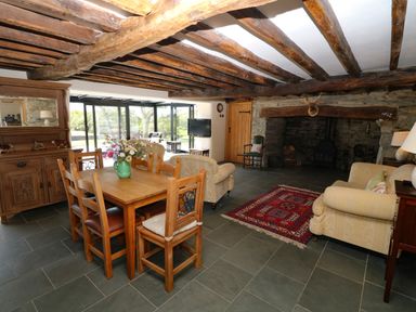 A living room with wooden beams, a dining table with chairs, sofas, a fireplace, and a cabinet at Garth Morthin The Farmhouse in Porthmadog