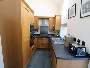 A kitchen with wooden cabinets black countertop a sink toaster and framed photos on the wall at Garth Morthin The Farmhouse in Porthmadog
