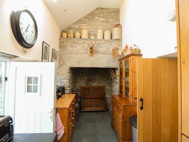 A kitchen with wooden cabinets, a stone fireplace, a mounted deer head, and pottery on a shelf at Garth Morthin The Farmhouse in Porthmadog