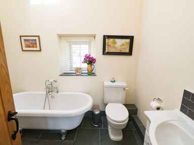 A bathroom with a clawfoot bathtub a toilet a sink and framed pictures on the walls at Garth Morthin The Farmhouse in Porthmadog