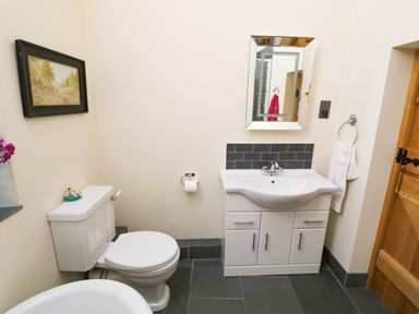 A bathroom with a toilet, sink with cabinet, mirror, towel ring with towel, and a framed painting at Garth Morthin The Farmhouse in Porthmadog