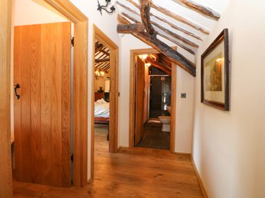 A hallway with wooden floors and beams leading to a bedroom and bathroom at Garth Morthin The Farmhouse in Porthmadog