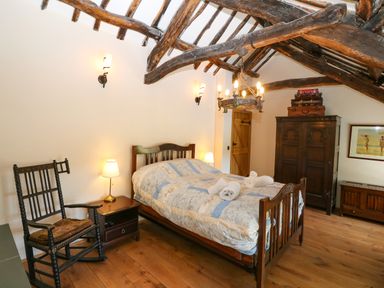 A bedroom with a wooden bed with folded towels a rocking chair a wooden wardrobe and exposed wooden ceiling beams at Garth Morthin The Farmhouse in Porthmadog