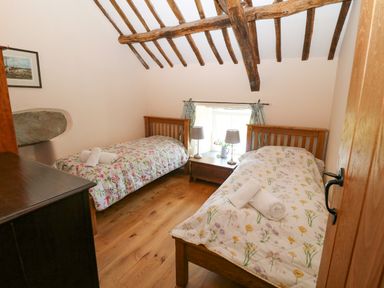 A bedroom with two single beds with floral bedspreads a wooden floor a window with curtains and wooden ceiling beams at Garth Morthin The Farmhouse in Porthmadog
