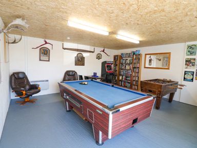 A game room with a pool table foosball table bookshelf armchairs and arcade machine at Garth Morthin The Farmhouse in Porthmadog
