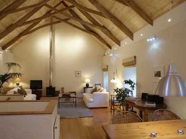 A living room with wooden beams on the ceiling sofas a wood stove and a dining table at The Barn in Aveton Gifford