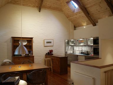 A kitchen and dining area with wooden ceiling beams and furniture at The Barn in Aveton Gifford