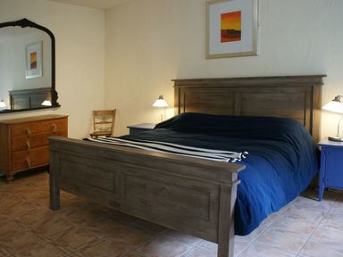 A bedroom with a wooden bed with blue bedding two bedside tables with lamps a wooden dresser with a mirror and a wooden chair at The Barn in Aveton Gifford