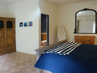 A bedroom with a wooden wardrobe blue bedding striped blanket on bed a dresser with a mirror and a standing mirror at The Barn in Aveton Gifford