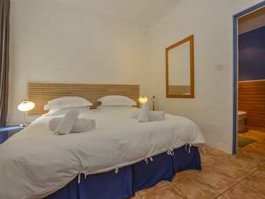 A bedroom with a double bed white bedding bedside lamps mirror and an adjacent bathroom at The Barn in Aveton Gifford