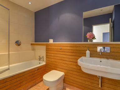 A bathroom with a bathtub toilet sink and mirror with flowers on the shelf at The Barn in Aveton Gifford