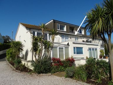 A two story house with a balcony and garden with plants and trees at 3 Tarifa in Bigbury-on-Sea