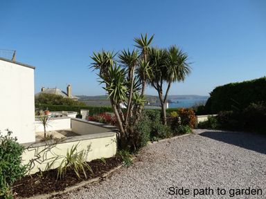 A side path with gravel and plants leading to a garden with palm trees near a house at 3 Tarifa in Bigbury-on-Sea