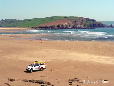 A lifeguard vehicle on a sandy beach near the sea with green hills in the background at Bigbury-on-Sea