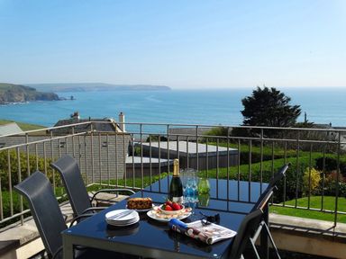 A balcony with a glass table and four chairs overlooking the sea at 3 Tarifa in Bigbury-on-Sea