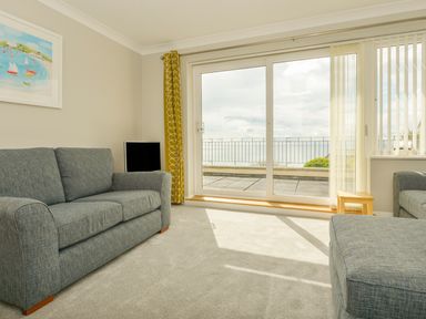 A living room with two gray sofas a small wooden table a TV and large sliding glass doors overlooking a balcony and sea at 3 Tarifa in Bigbury-on-Sea