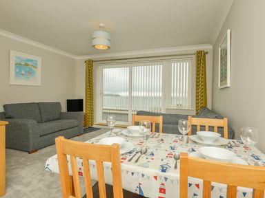 A living room with two sofas a dining table set for four and sliding glass doors with vertical blinds at 3 Tarifa in Bigbury-on-Sea