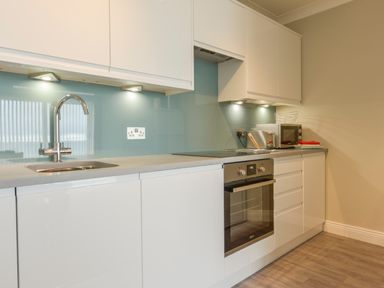 A modern kitchen with white cabinets a stainless steel sink an oven a microwave and under cabinet lighting at 3 Tarifa in Bigbury-on-Sea