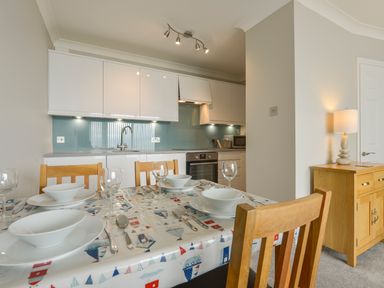 A kitchen with white cabinets a dining table set with plates bowls and glasses and a wooden sideboard with a lamp at 3 Tarifa in Bigbury-on-Sea
