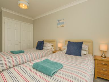 A bedroom with two single beds striped bedding blue pillows wooden nightstands and lamps at 3 Tarifa in Bigbury-on-Sea