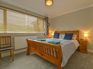 A bedroom with a wooden bed frame two bedside tables with lamps a chair and a window with blinds at 3 Tarifa in Bigbury-on-Sea