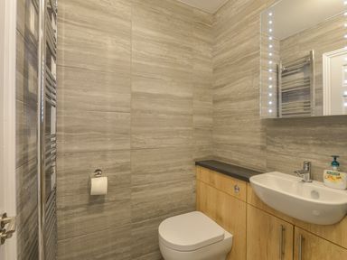 A bathroom with a toilet sink wooden cabinets mirror and wall-mounted toilet paper holder at 3 Tarifa in Bigbury-on-Sea